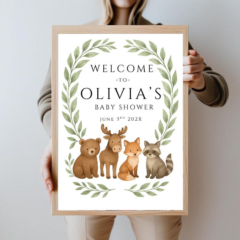 May include: Welcome to Olivia's Baby Shower sign with a green leafy wreath and woodland animals including a bear, moose, fox, and raccoon. The date is June 3rd, 202X.