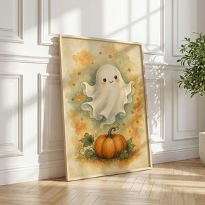 May include: A framed vertical wall art print featuring a watercolor illustration of a smiling white ghost floating above an orange pumpkin. The background is a soft blend of yellow and orange hues with small scattered stars throughout the composition.