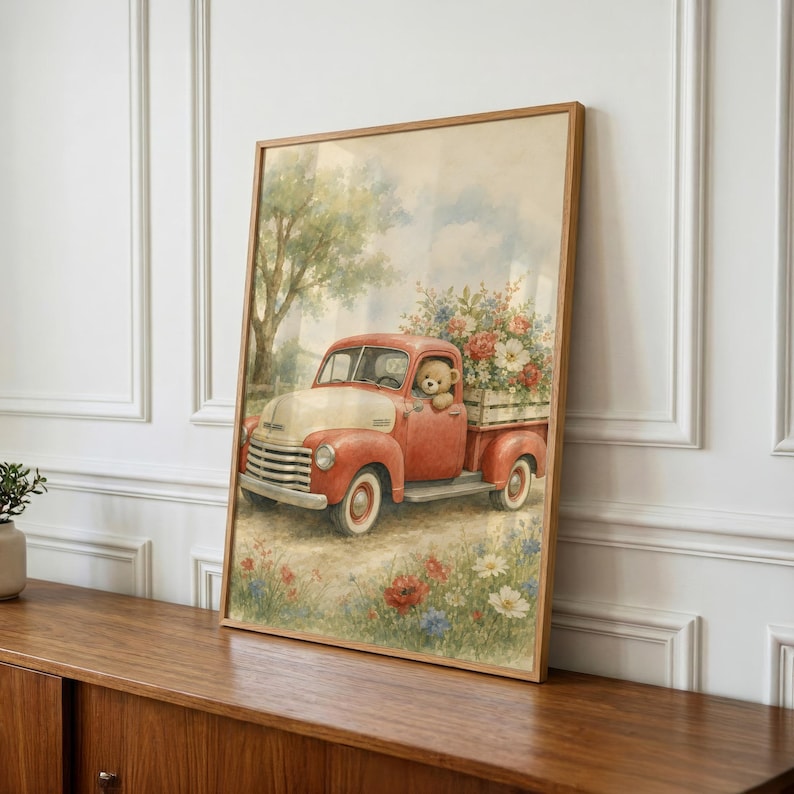 May include: A framed wall art print featuring a vintage red pickup truck with a cream-colored hood. A teddy bear sits in the driver seat, and the truck bed is filled with a large bouquet of colorful flowers. The scene is set in a field of wildflowers.