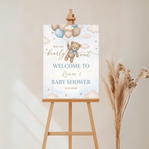 May include: A blue and white baby shower welcome sign with a teddy bear holding balloons. The sign reads "We can barely wait. Welcome to Liam's Baby Shower 6.23.202X".