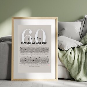 May include: A framed print with a beige background and white text. The print features the number 60 with the word "sixty" below it. The text "Reasons We Love You" is below the number. The print is surrounded by a wooden frame.