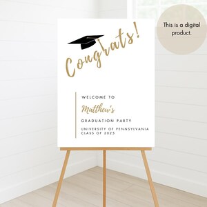 K&ouml;nnte beinhalten: Ein wei&szlig;es Schild mit goldener Schrift, auf dem "Herzlichen Gl&uuml;ckwunsch!" steht, mit einer schwarzen Studentenm&uuml;tze &uuml;ber dem Text. Das Schild sagt auch "Willkommen zur Abschlussfeier von Matthew, University of Pennsylvania, Klasse von 2025".