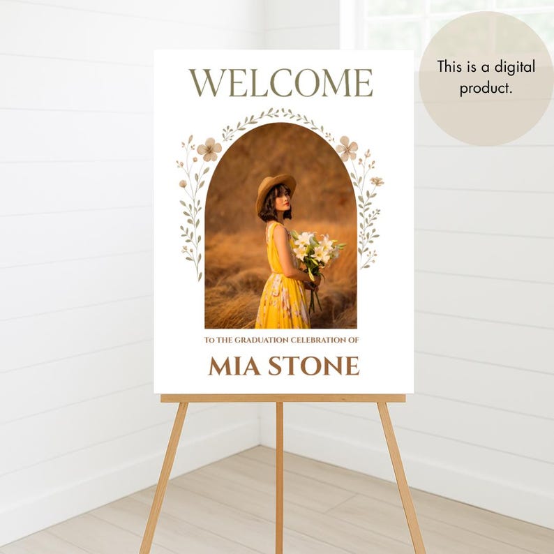 May include: A white welcome sign with a floral archway and a photo of a woman in a yellow dress. The text "WELCOME" is at the top of the sign, and the text "TO THE GRADUATION CELEBRATION OF MIA STONE" is at the bottom.