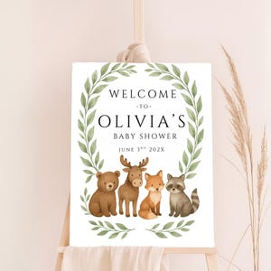 May include: Welcome to Olivia's Baby Shower sign with a green leafy wreath and four woodland animals: a bear, moose, fox, and raccoon. The date is June 3rd, 202X.