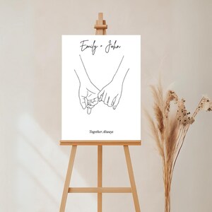 以下が含まれることがあります： 2つの手が絡み合った白黒の線画で、画像の下に「Emily + John」と「Together Always」のテキストがあります。