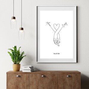 May include: A black and white line drawing of two hands holding each other, with a heart shape in the middle. The names "Anna" and "Casey" are written above the hands, with arrows pointing towards them. The text "You & Me" is written below the hands.