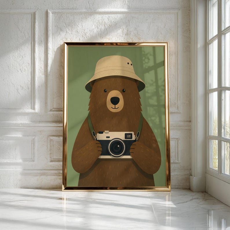 May include: A framed wall art print featuring a brown bear wearing a beige bucket hat and holding a vintage-style camera. The bear is centered against a solid olive green background, and the artwork is enclosed in a thin metallic gold frame.