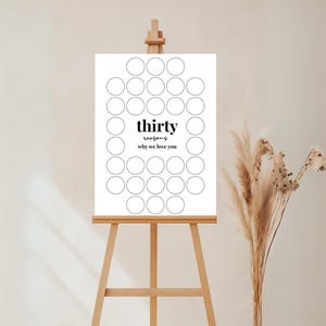 以下が含まれることがあります： 木製のイーゼルに置かれた白い看板。黒字で「thirty reasons why we love you」と書かれています。理由を書くための30個の円があります。右側の花瓶にはドライフラワーが入っています。