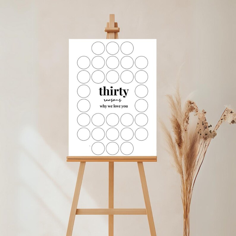 以下が含まれることがあります： 木製のイーゼルに置かれた白い看板。黒字で「thirty reasons why we love you」と書かれています。理由を書くための30個の円があります。右側の花瓶にはドライフラワーが入っています。