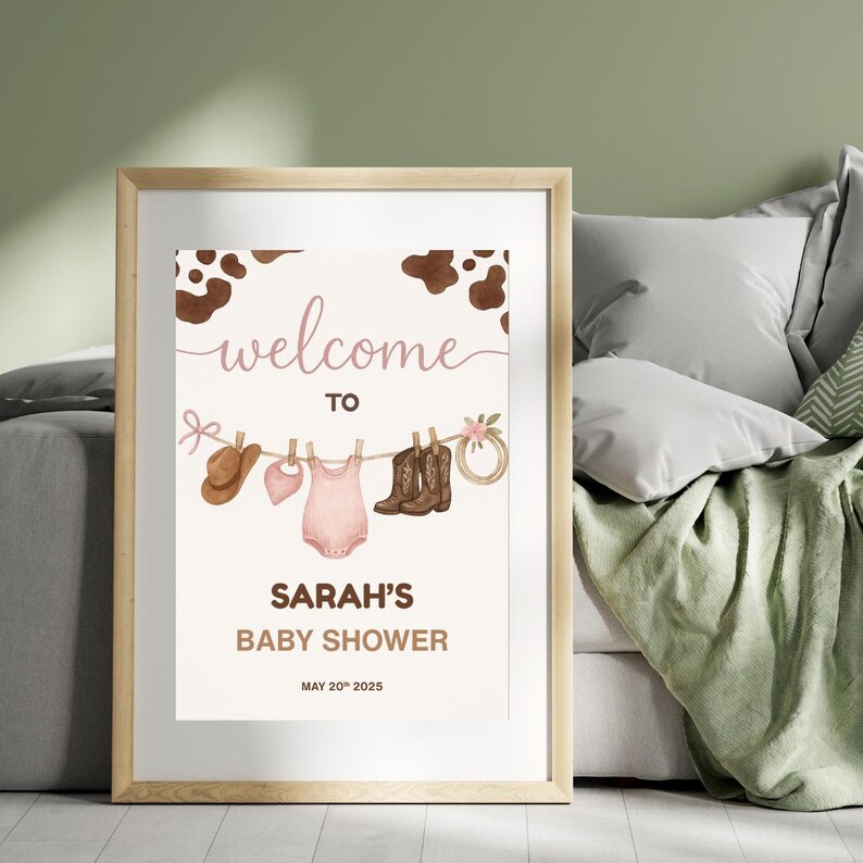 Może przedstawiać: Witamy na Baby Shower Sarah z brązowym tłem w kropki krowy. Na plakacie znajduje się sznurek do suszenia z r&oacute;żowym body dla niemowlęcia, r&oacute;żowym śliniakiem, brązowym kowbojskim kapeluszem i dwiema parami brązowych kowbojskich but&oacute;w.