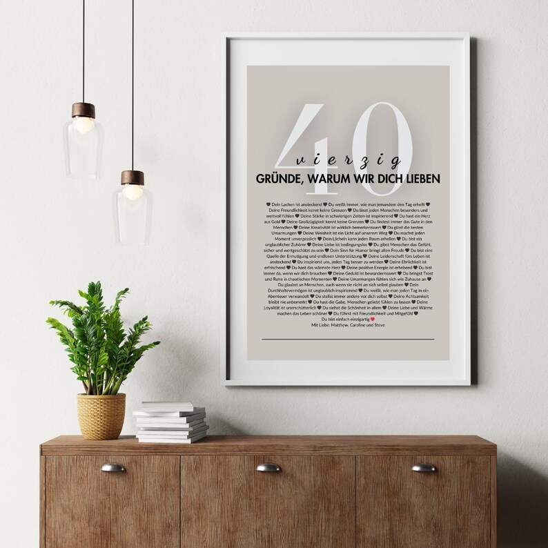 Puede incluir: Una impresi&oacute;n enmarcada con un borde blanco presenta el n&uacute;mero "40" y las palabras alemanas "vierzig Gr&uuml;nde, warum wir dich lieben" en una fuente gris claro. El texto de abajo enumera 40 razones en alem&aacute;n. La impresi&oacute;n se muestra en un mueble de madera.