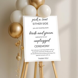 May include: White sign with black text on an easel. The sign reads "pick a seat either side you are loved by both bride and groom welcome to our unplugged ceremony we invite you to be fully present with us during the ceremony. Kindly turn off all cell phones and cameras and enjoy this special moment with us. thank you!"