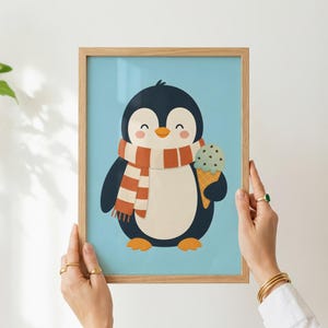 May include: A framed wall art print featuring a cartoon penguin with a black and white body, an orange beak, and rosy cheeks. The penguin wears an orange and white striped scarf and holds a chocolate chip ice cream cone against a light blue background.