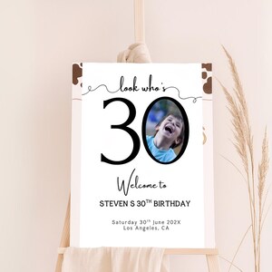 Peut inclure: Panneau de bienvenue blanc sur chevalet, avec l'inscription "look who's 30 Welcome to STEVEN S 30TH BIRTHDAY" et une photo d'un enfant riant. La date et le lieu sont &eacute;galement indiqu&eacute;s.