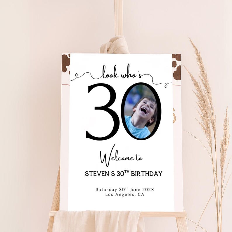 Peut inclure: Panneau de bienvenue blanc sur chevalet, avec l'inscription "look who's 30 Welcome to STEVEN S 30TH BIRTHDAY" et une photo d'un enfant riant. La date et le lieu sont &eacute;galement indiqu&eacute;s.