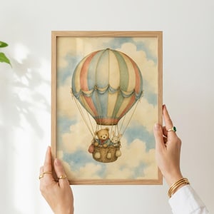 Może przedstawiać: Oprawiony wydruk w stylu akwareli przedstawiający balon na ogrzane powietrze w pionowe pasy w stonowanych kolorach niebieskim, czerwonym i kremowym. Pluszowy miś i mały kr&oacute;liczek siedzą w wiklinowym koszu zawieszonym pod balonem na tle nieba.