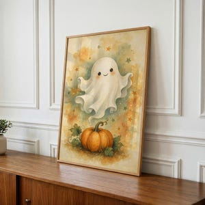 May include: A framed watercolor-style print featuring a smiling white ghost floating above a round orange pumpkin. The background is a soft blend of yellow, orange, and green hues decorated with small scattered stars, all enclosed in a light wood frame.
