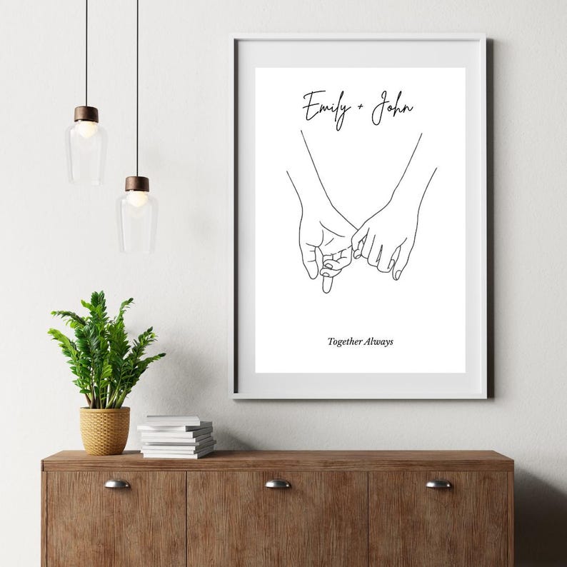 以下が含まれることがあります： 2つの手が小指を絡ませている白黒の線画プリント。プリントには「Emily + John」と「Together Always」のテキストが含まれています。