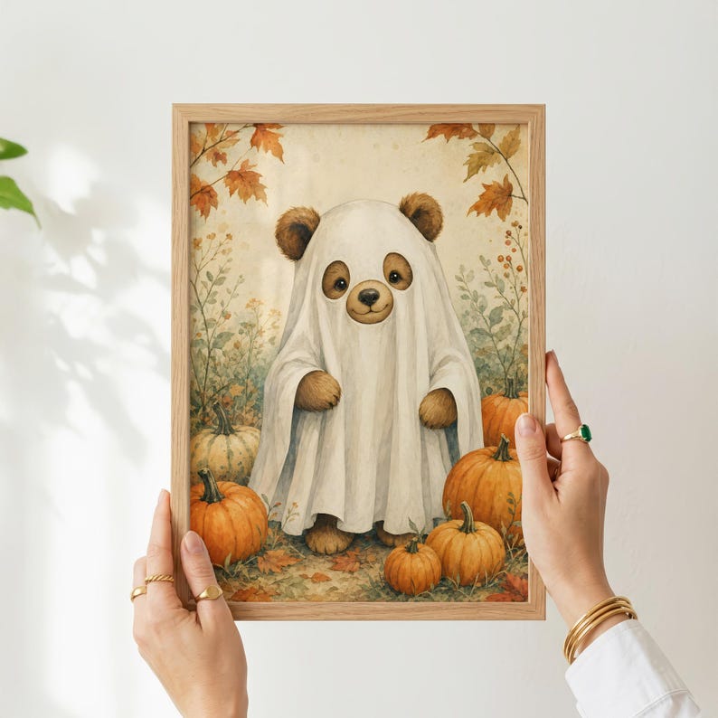 May include: A framed wall art print featuring a brown bear wearing a white ghost costume, standing in a field of orange pumpkins and autumn leaves. The illustration uses soft, warm tones to depict the bear and the surrounding fall harvest scene.