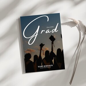 Pode incluir: Um cart&atilde;o de an&uacute;ncio de gradua&ccedil;&atilde;o com uma silhueta de um grupo de pessoas usando toucas e becas de gradua&ccedil;&atilde;o contra um c&eacute;u de p&ocirc;r do sol. O texto "Grad" est&aacute; escrito em uma fonte branca cursiva com o texto "Class of 2023" abaixo. O nome "MARY JOHNSON" e "MALIBU HIGH SCHOOL" est&atilde;o impressos abaixo da imagem.