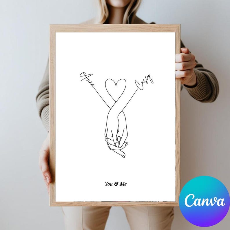 May include: A printable art print with a minimalist line drawing of two hands holding each other, forming a heart shape. The names "Anna" and "Casey" are written above the hands, and the text "You & Me" is written below. The print is framed in a light wood frame.