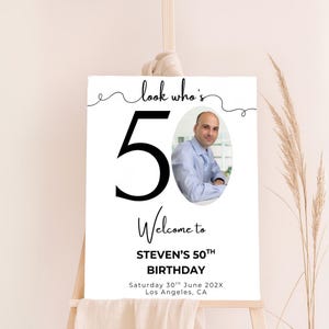 May include: A white sign with black text and a photo of a man. The sign says "Look who's 50. Welcome to Steven's 50th Birthday. Saturday 30th June 202X. Los Angeles, CA."