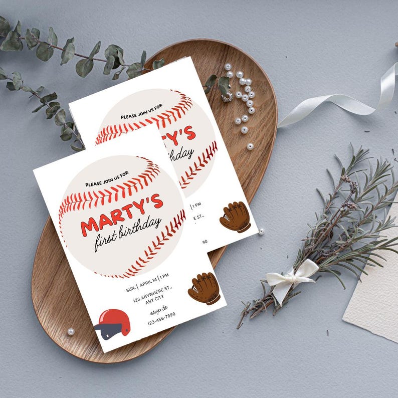K&ouml;nnte beinhalten: Zwei Baseball-Motto-Geburtstagseinladungen mit einer roten und wei&szlig;en Baseball-Grafik und dem Text "Marty's first birthday". Die Einladungen liegen auf einer Holzoberfl&auml;che mit wei&szlig;em Band und Gr&uuml;n.