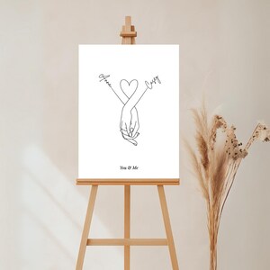May include: A black and white line drawing of two hands intertwined with a heart in the middle. The names "Anna" and "Casey" are written above the hands. The text "You & Me" is written below the hands.