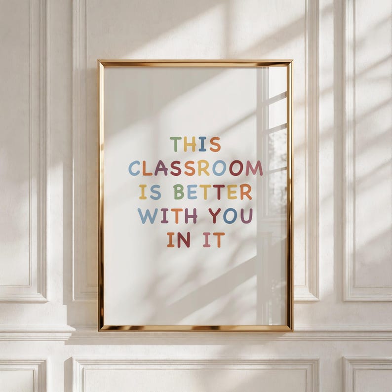 May include: A vertical rectangular wall art print in a thin gold frame featuring the multicolored text THIS CLASSROOM IS BETTER WITH YOU IN IT centered on a white background. The letters are rounded and appear in shades of blue, red, and yellow.