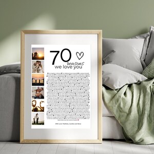 Pode incluir: Uma impress&atilde;o emoldurada com o texto "70 raz&otilde;es pelas quais te amamos" em preto. A impress&atilde;o inclui v&aacute;rias fotos pequenas e uma lista de raz&otilde;es. A moldura &eacute; de cor de madeira clara, e o fundo inclui almofadas e um cobertor.