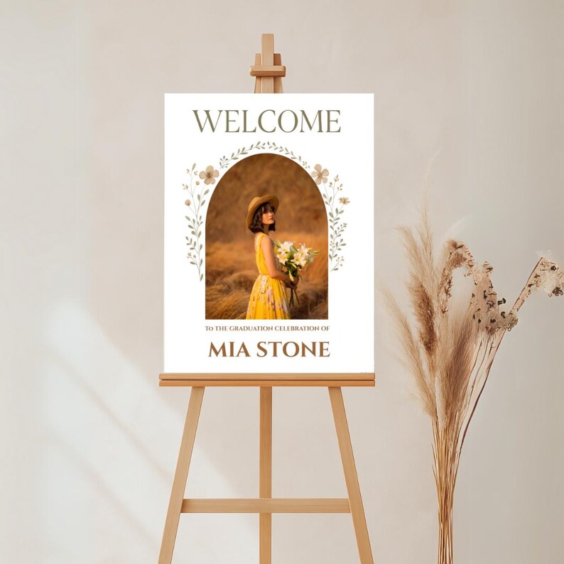 May include: Welcome sign with a floral arch and a photo of a woman in a yellow dress. The sign reads "Welcome to the graduation celebration of Mia Stone".