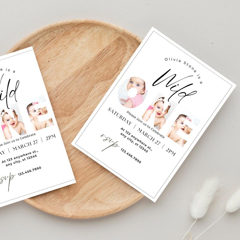 May include: Two white invitation cards with a baby's photo and the text "Olivia Stone is a Wild" on a wooden tray. The cards include event details: Saturday, March 27, 2 PM, and an RSVP section with a phone number.