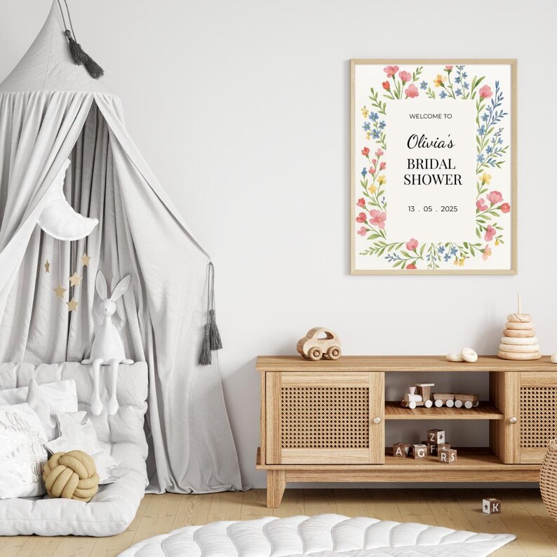 May include: A floral-themed bridal shower sign with the text "Welcome to Olivia's Bridal Shower 13.05.2025". The sign is framed in a light wood frame and is hanging on a white wall.
