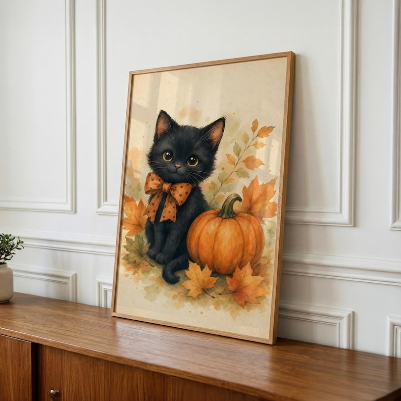 May include: A framed watercolor-style print featuring a fluffy black kitten with large eyes wearing an orange polka-dot bow tie. The kitten sits beside a round orange pumpkin surrounded by scattered autumn leaves in shades of gold and brown.