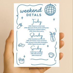 May include: A white card with blue text and illustrations, held by a hand. The card reads "weekend DETAILS" and lists a schedule of events for Friday, Saturday, and Sunday, including check-in, drinks, dinner, and activities.