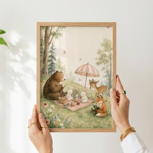 May include: A framed rectangular print featuring a watercolor illustration of a brown bear, two white rabbits, a fawn, and a fox having a picnic on a red and white checkered blanket under a striped umbrella in a forest setting with wildflowers.