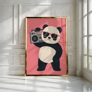 May include: A framed wall art print featuring a cartoon panda with black and white fur, wearing pink sunglasses, and holding a grey boombox on its shoulder. The panda is centered against a solid pink background within a thin gold frame.