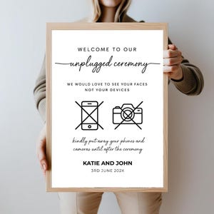 Puede incluir: Un cartel blanco con texto negro e iconos que dice "Bienvenido a nuestra ceremonia desconectada. Nos encantar&iacute;a ver sus caras, no sus dispositivos." Tambi&eacute;n tiene un icono de tel&eacute;fono y c&aacute;mara tachados. El cartel tambi&eacute;n dice "Por favor, guarde sus tel&eacute;fonos y c&aacute;maras hasta despu&eacute;s de la ceremonia." El cartel est&aacute; firmado "Katie y John" y la fecha "3 de junio de 202X".