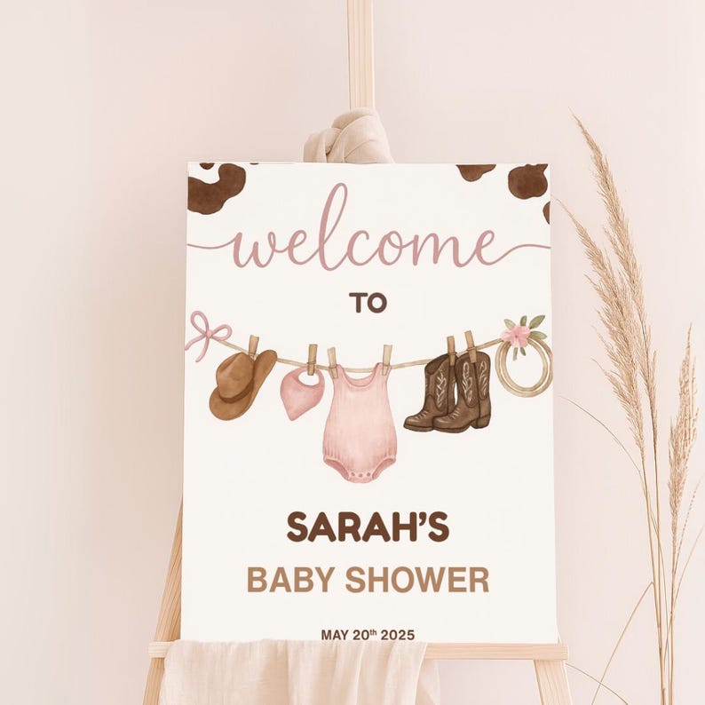 Może przedstawiać: Tablica powitalna na baby shower Sarah z brązowym tłem w kratę krowią. Na tablicy znajduje się r&oacute;żowy śpioszek dla niemowlęcia, brązowy kowbojski kapelusz i para brązowych kowbojskich but&oacute;w wiszących na sznurku do suszenia ubrań z r&oacute;żowymi kwiatami. Data baby shower to 20 maja 2025.