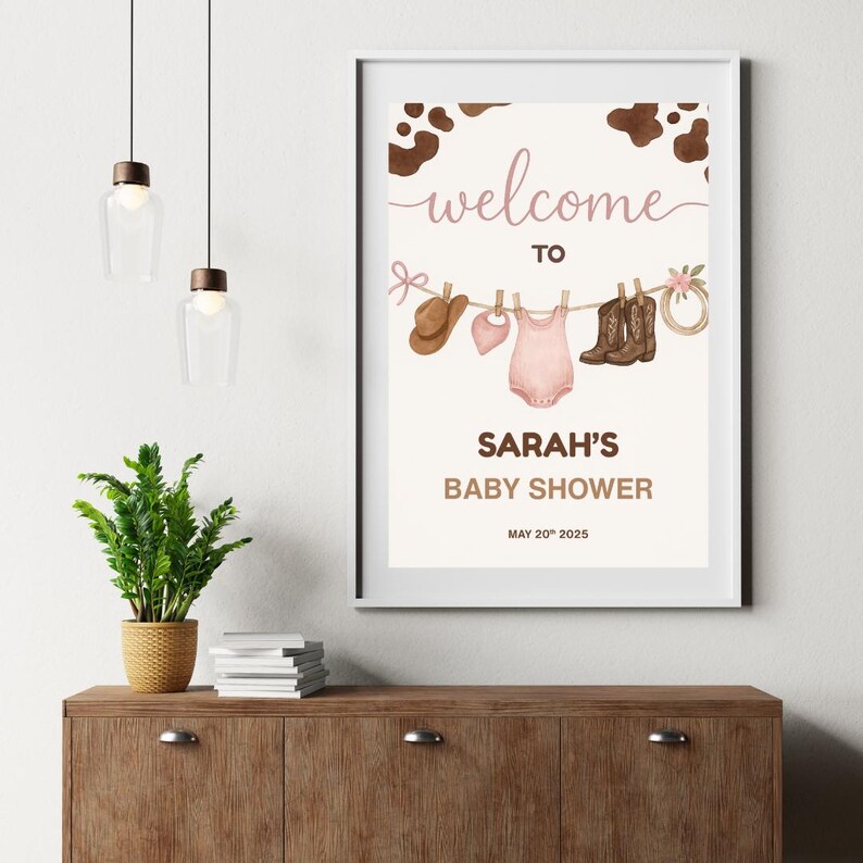 Może przedstawiać: Drukowana tablica powitalna na baby shower z brązowym tłem w kratę krowią. Tablica przedstawia sznurek do suszenia z r&oacute;żowym body dla dziecka, brązowym kowbojskim kapeluszem, r&oacute;żowym śliniakiem, brązowymi kowbojskimi butami i brązowym sznurkiem z r&oacute;żową kokardką. Tekst na tablicy brzmi "Witamy na baby shower Sarah 20 maja 2025".