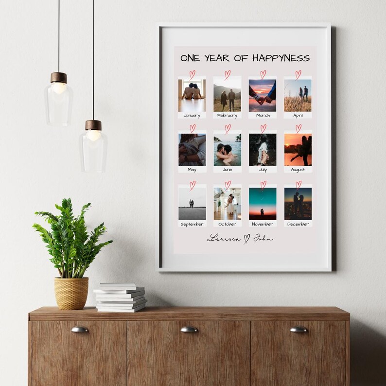 May include: A framed print with a pink background and white border. The print features a collage of 12 polaroid-style photos of a couple throughout the year, with each photo labeled with a month. The text "ONE YEAR OF HAPPYNESS" is at the top of the print, and the names "Lerissa & John" are at the bottom.