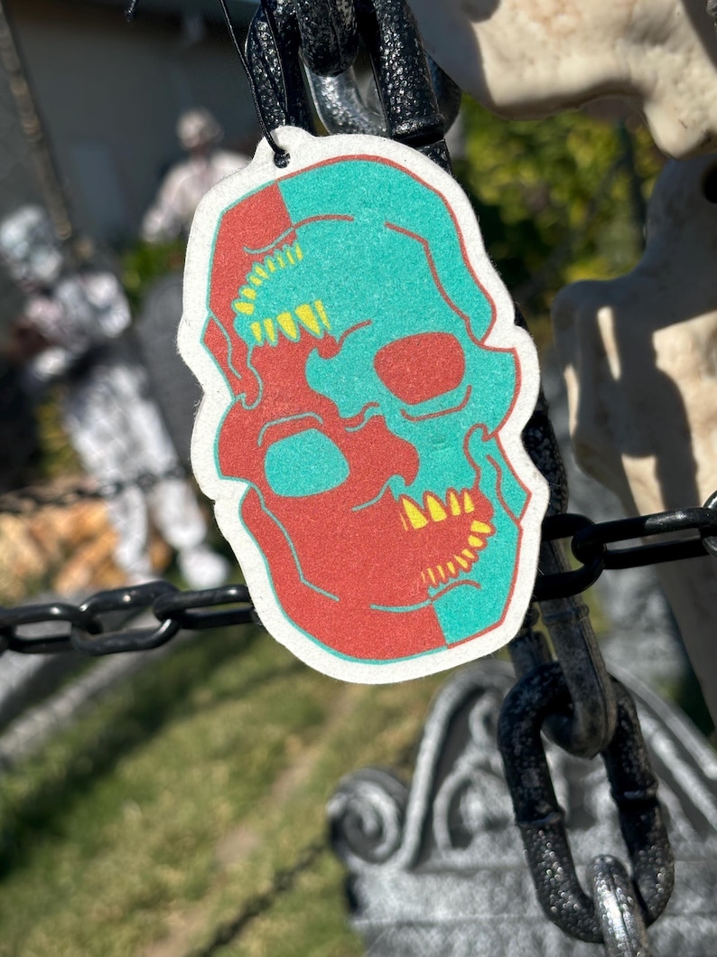 May include: A red and teal skull car air freshener with yellow teeth. The skull is split down the middle, with one side red and the other teal.