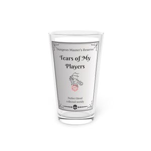 Könnte beinhalten: Ein klares Glas mit einem weißen Etikett, auf dem "Dungeon Master's Reserve Tears of My Players" steht. Das Etikett zeigt auch eine Schwarzweißillustration eines Drachen und eines roten 20-seitigen Würfels.