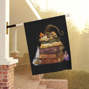 Peut inclure: Drapeau d'extérieur noir avec une pile de livres intitulés "Grimoire", "Remèdes" et "Protection". Un chapeau de sorcière, une citrouille et des feuilles d'automne sont posés sur les livres. Une plume et un encrier sont à gauche, et une fiole de potion à droite.