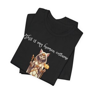 May include: Black t-shirt with a white cat wearing a white robe and holding a staff. The text "This is my human costume" is printed on the shirt.