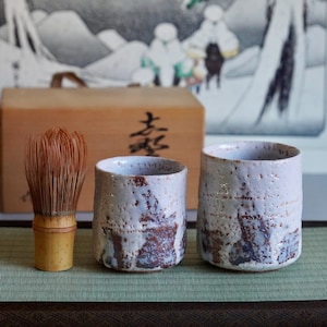 Puede incluir: Un juego de tres tazas de cerámica con un acabado mate moteado. Las tazas son de color crema, gris claro y gris oscuro. Cada taza tiene un diseño simple y minimalista y un asa redondeada.