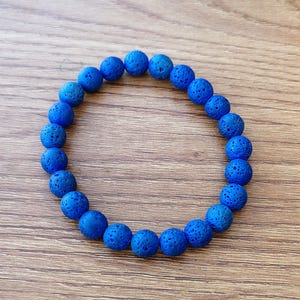 Puede incluir: Una pulsera circular compuesta por numerosas cuentas esféricas de piedra volcánica de color azul vibrante y porosas. Las cuentas están ensartadas en un bucle continuo, mostrando una superficie texturizada y picada en cada cuenta.
