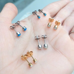 May include: A set of six stud earrings with different coloured stones. The earrings are made of stainless steel and have a simple design. The stones are blue, white, and gold.