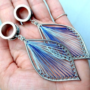 May include: A pair of silver ear gauges with blue and white thread designs. The gauges are circular and have a smooth, polished finish.