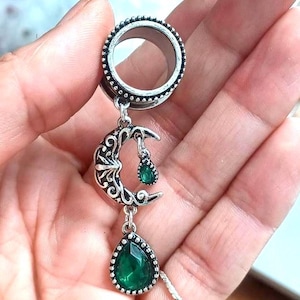 May include: Silver ear gauge with a crescent moon charm and two dangling green gem stones.